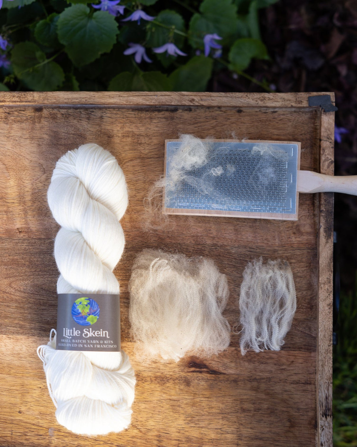 Wound skein of undyed yarn with representative samples of the fiber contained in the yarn: merino wool. A wool carding brush is also shown.