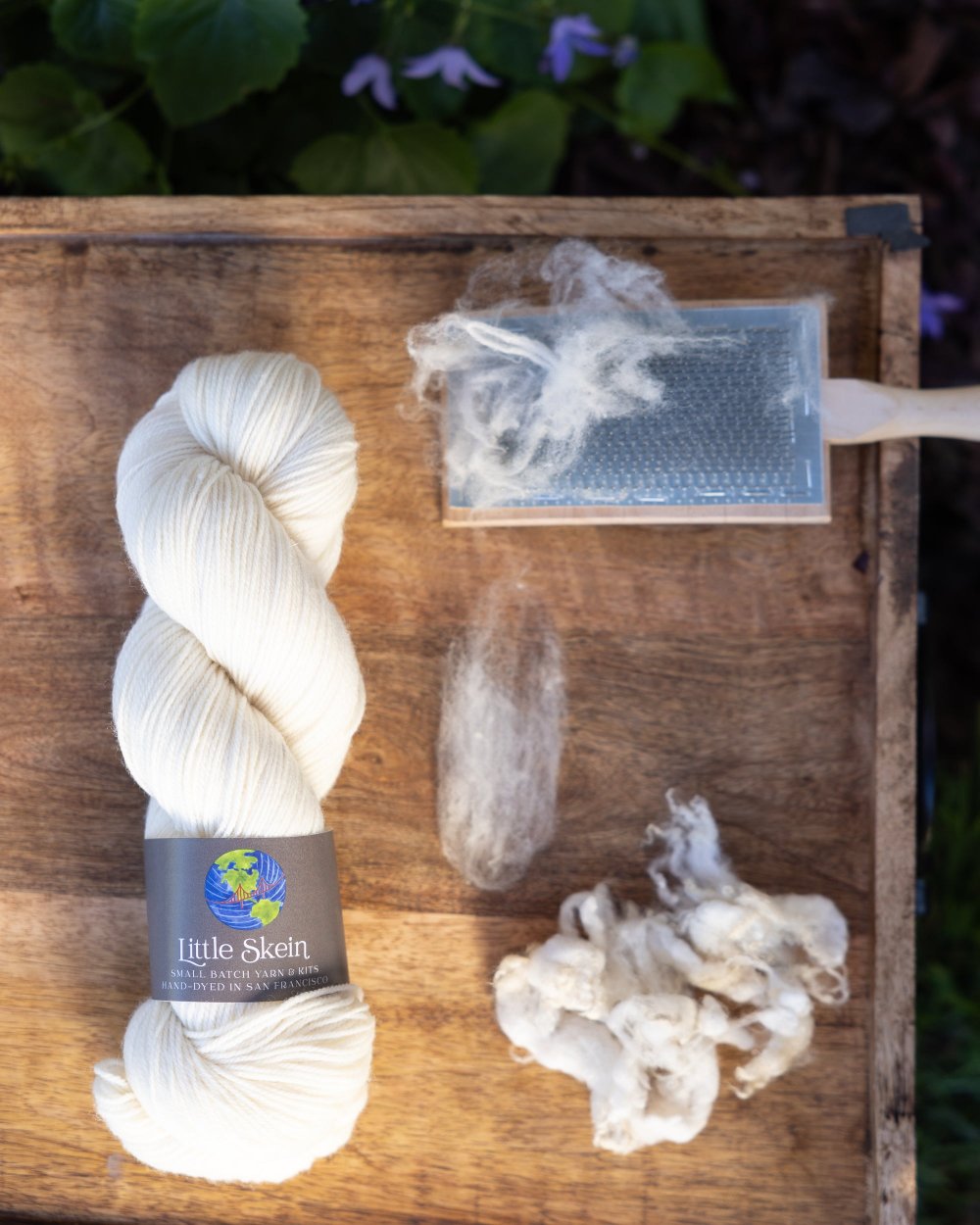 Wound skein of undyed yarn with representative samples of the fiber contained in the yarn: targhee wool. A wool carding brush is also shown.