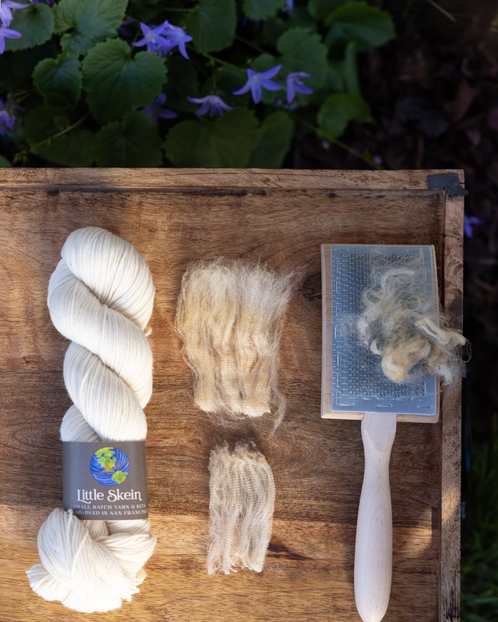 Wound skein of undyed yarn,representative samples of the fiber contained in the yarn: merino and rambouillet wool, and a carding brush with wool on top