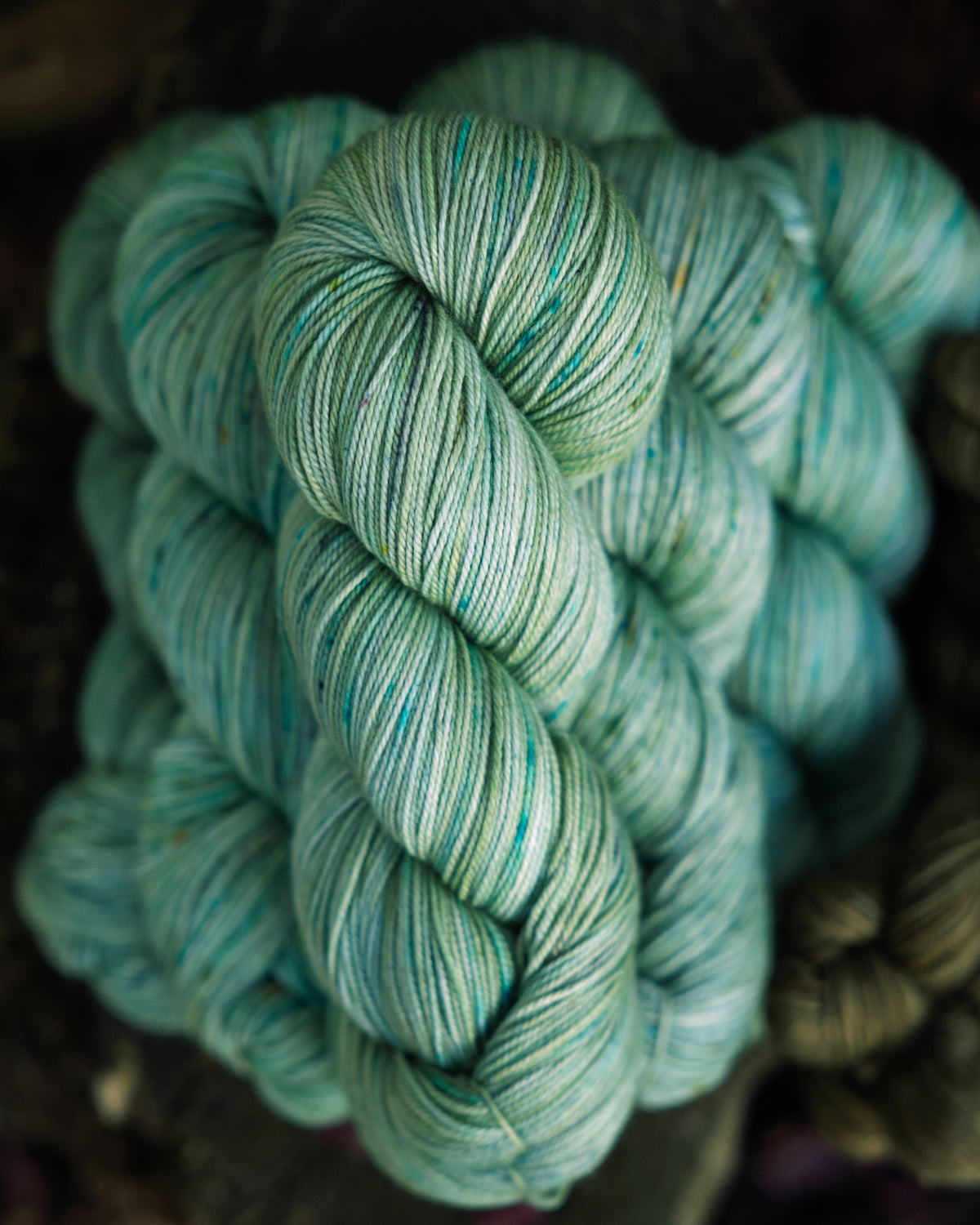 Stack of hand-dyed yarn in a soft green color, with blue and brown speckles