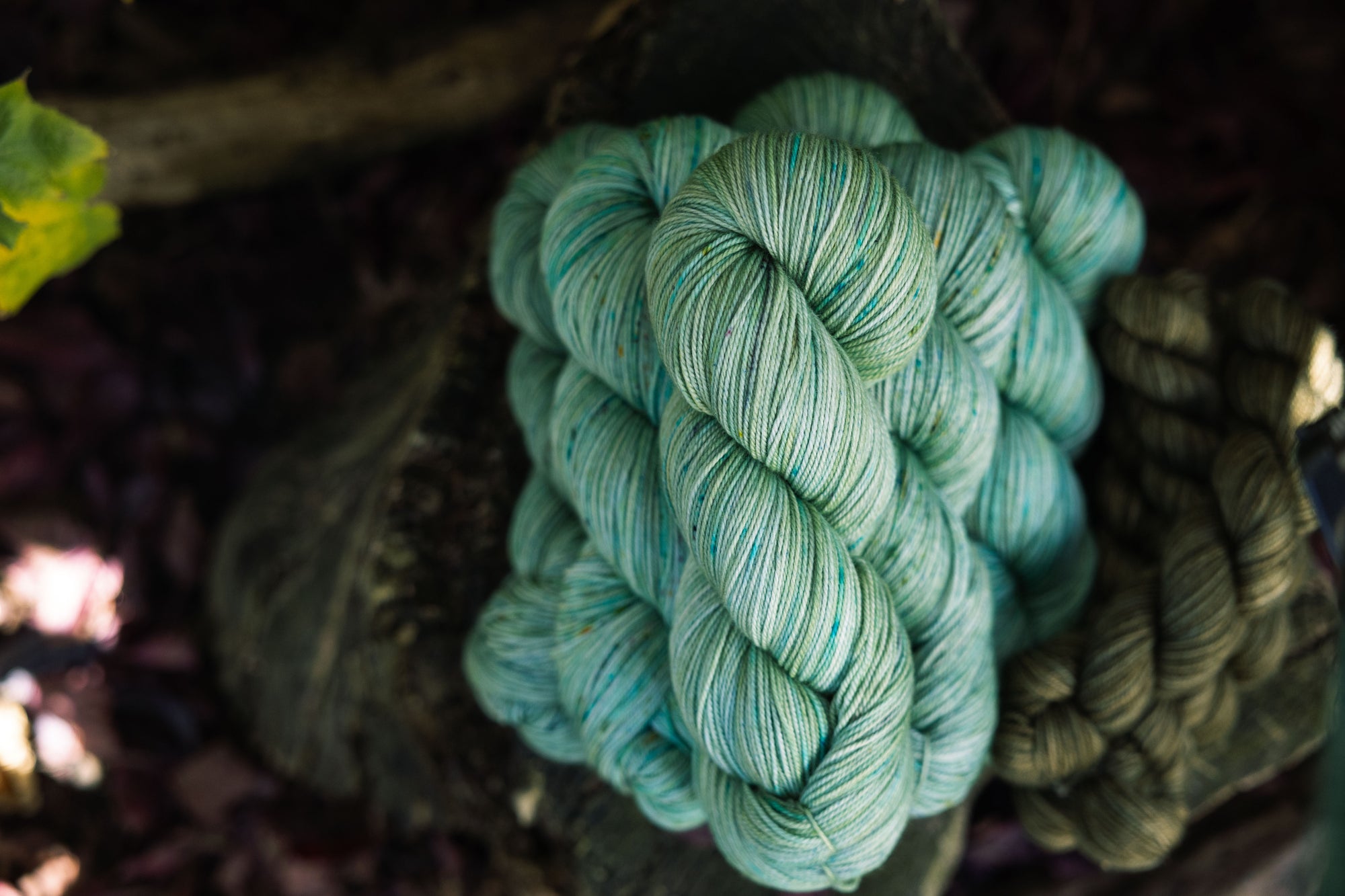 Stack of hand-dyed yarn in a soft green color, with blue and brown speckles