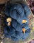 A small stack of deep blue colored hand-dyed yarn, placed on a wood stump and with yellow ginkgo leaves falling around it.