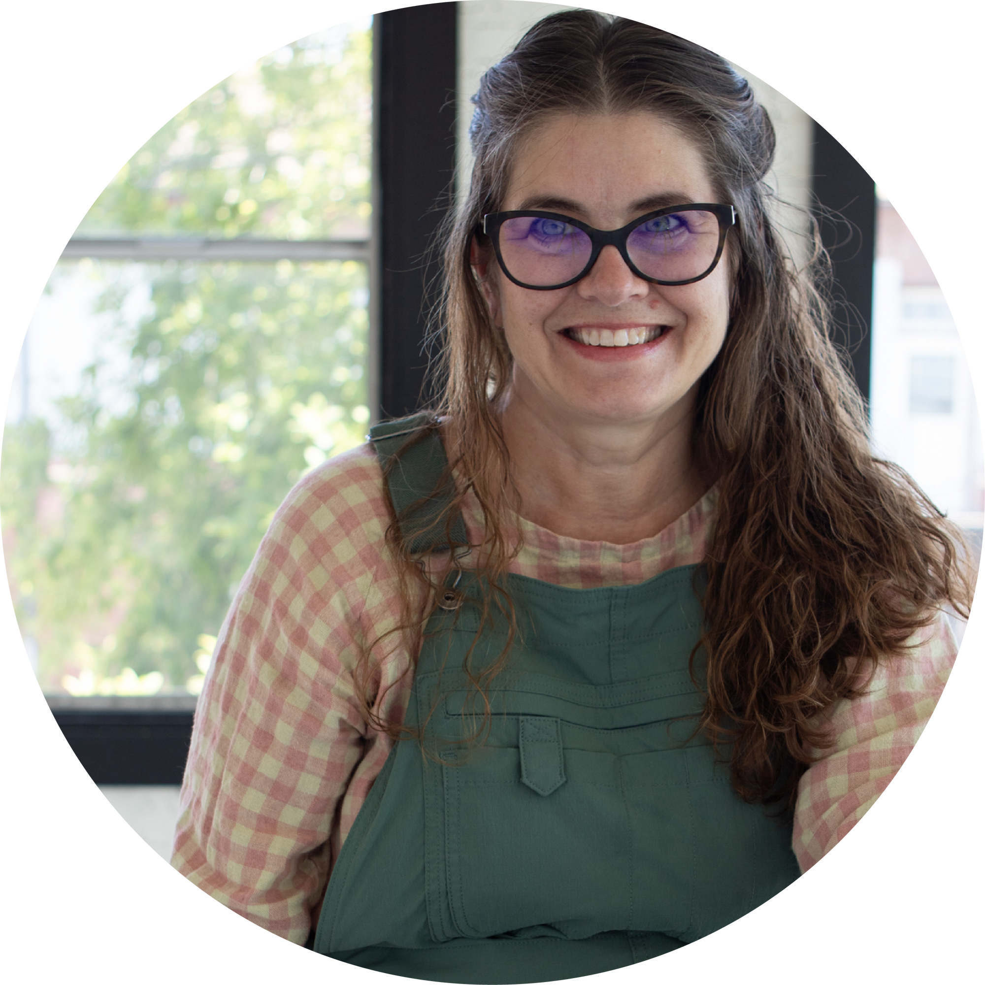 Anne, a white woman, is smiling at the camera and wearing overalls.