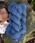 A small stack of deep blue colored hand-dyed yarn, placed on a wood stump and with bits of gingham fabric nearby