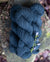 A small stack of deep blue colored hand-dyed yarn, placed on a wood stump and with a small purple flower nearby