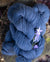 A small stack of deep blue-colored hand-dyed yarn, with a small purple flower nearby